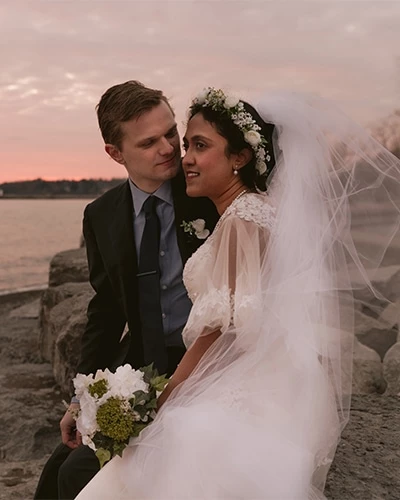 A groom gazes with love as his bride as they sit on a big stone near the Lake Ontario waterfront in Pickering, Ontario, Canada