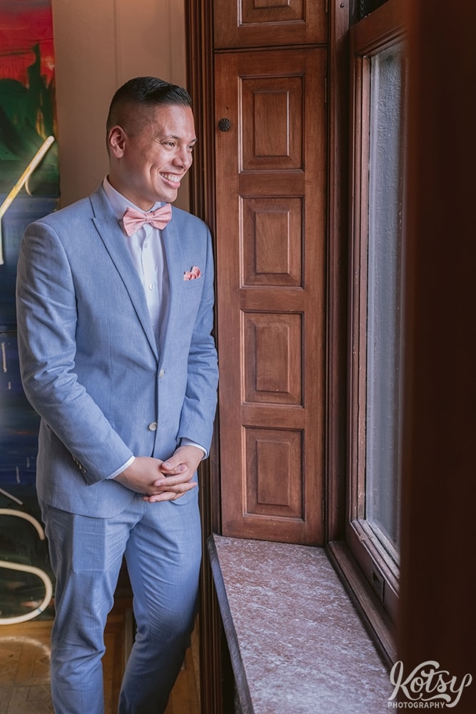 A groom laughs while looking out a window at Berkeley Bicycle Club in Toronto, Ontario