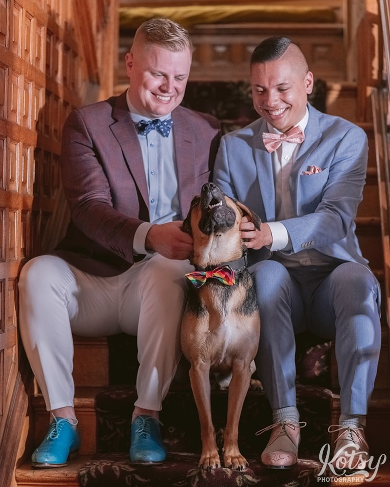 Two grooms play with their dog on a set of stairs at Berkeley Bicycle Club in Toronto, Ontario