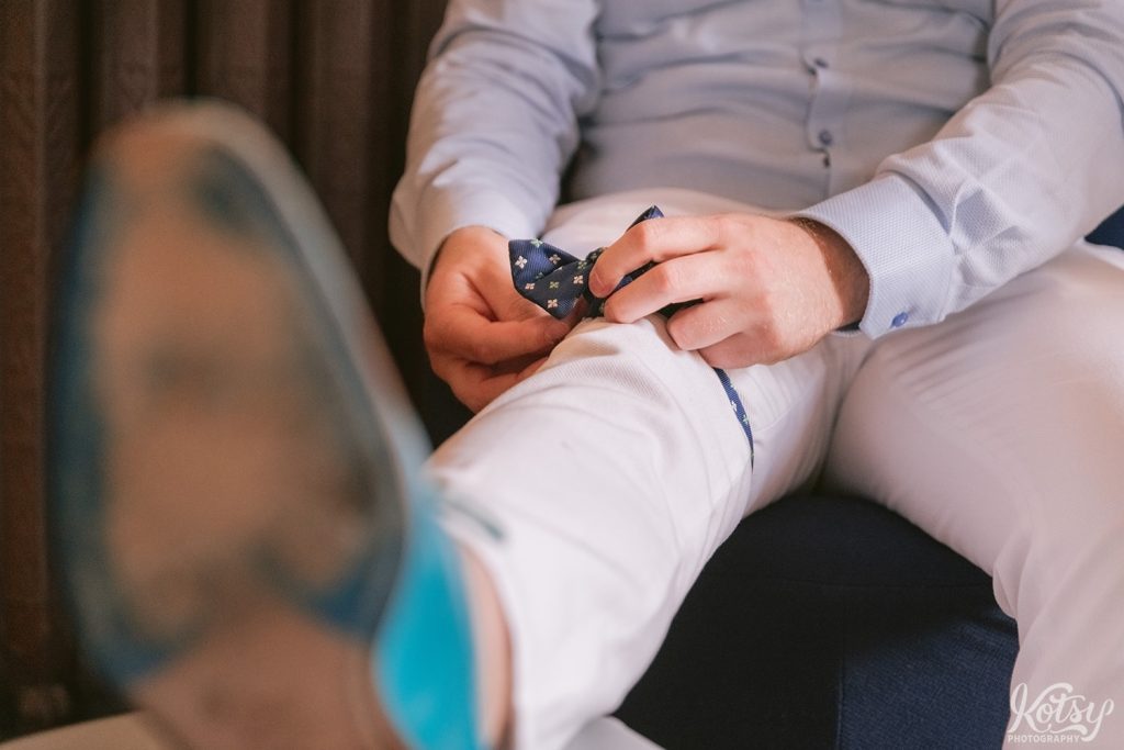 A groom pre-ties a bow-tie around his leg.