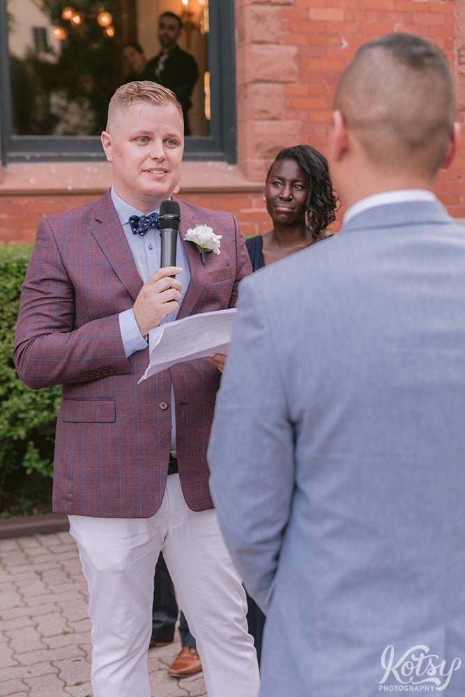 A groom reads his partner his vows at their outdoor wedding ceremony at Berkeley Bicycle Club in Toronto, Ontario