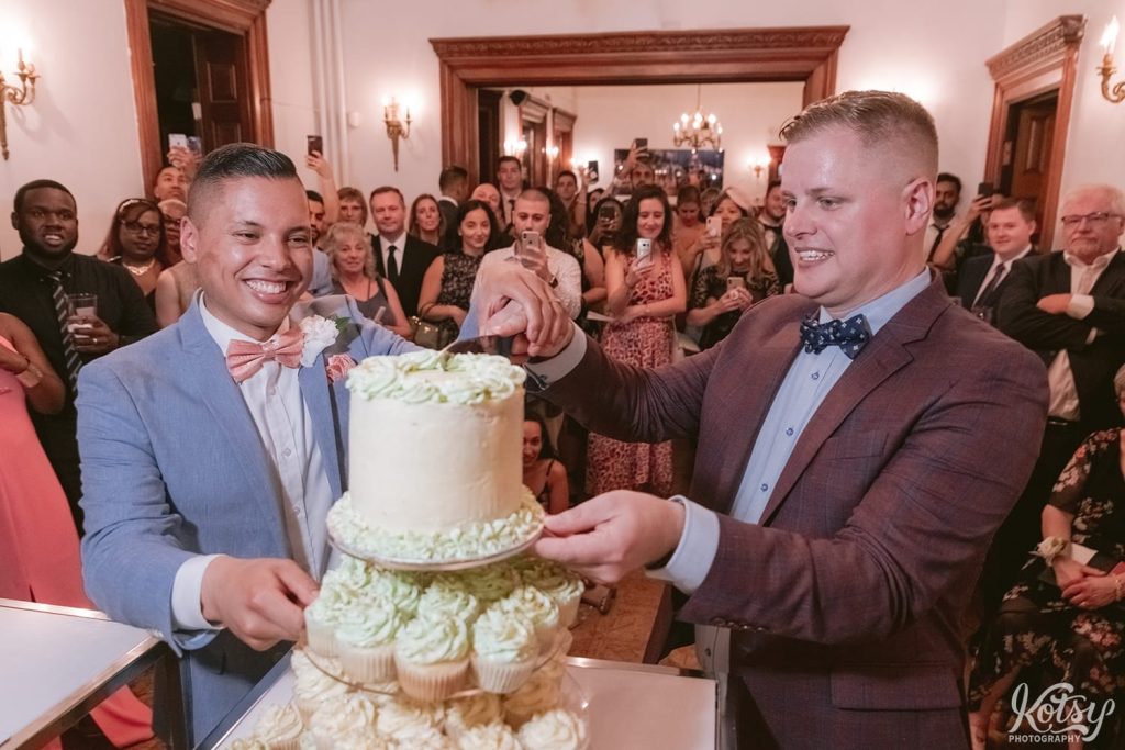 Two grooms cut their wedding cake during their wedding reception at Berkeley Bicycle Club in Toronto