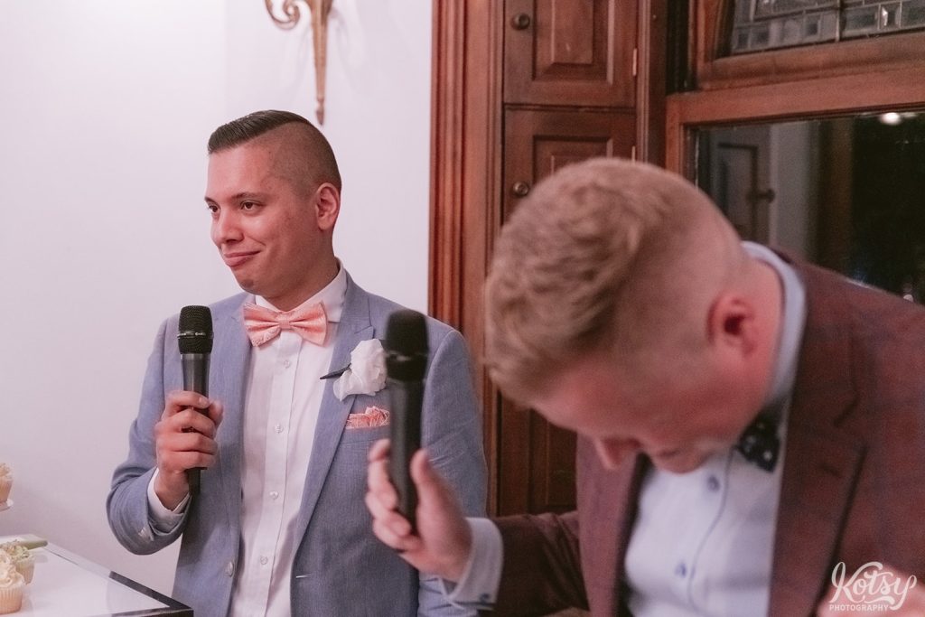 A groom smirks during his partner's speech during their wedding reception at Berkeley Bicycle Club in Toronto