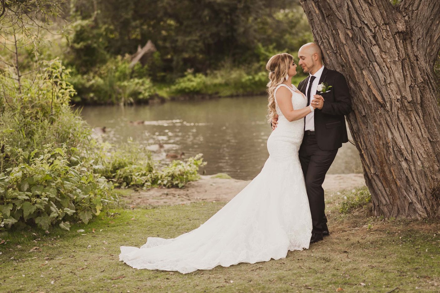 A bride and groom hold each other by a lake.