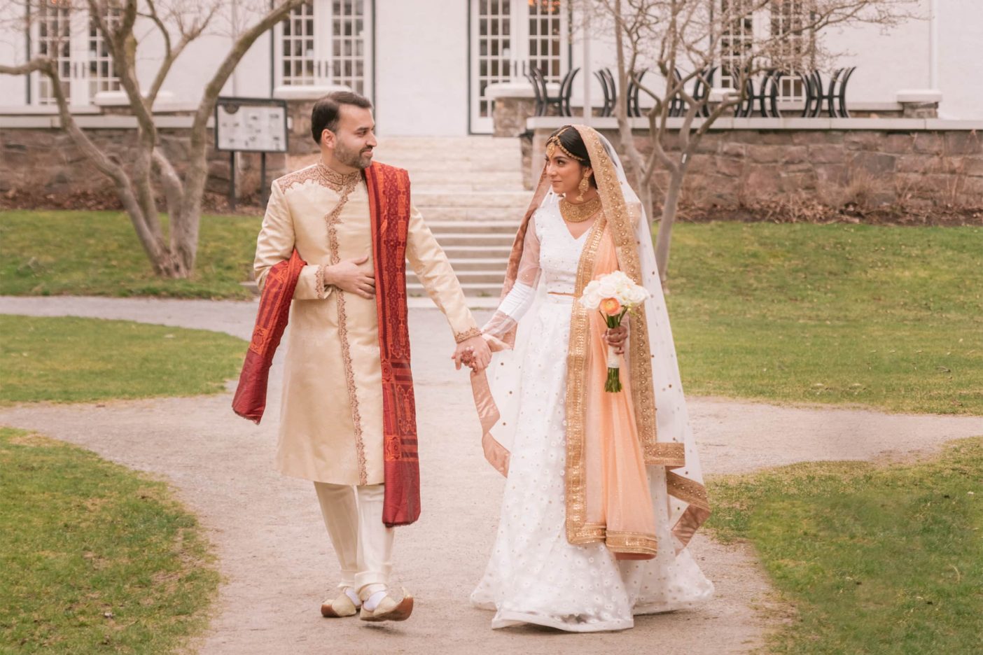 A bride and groom dressed in traditional south asian wedding attire go for a walk at Guild Inn Estate in Toronto, Ontario