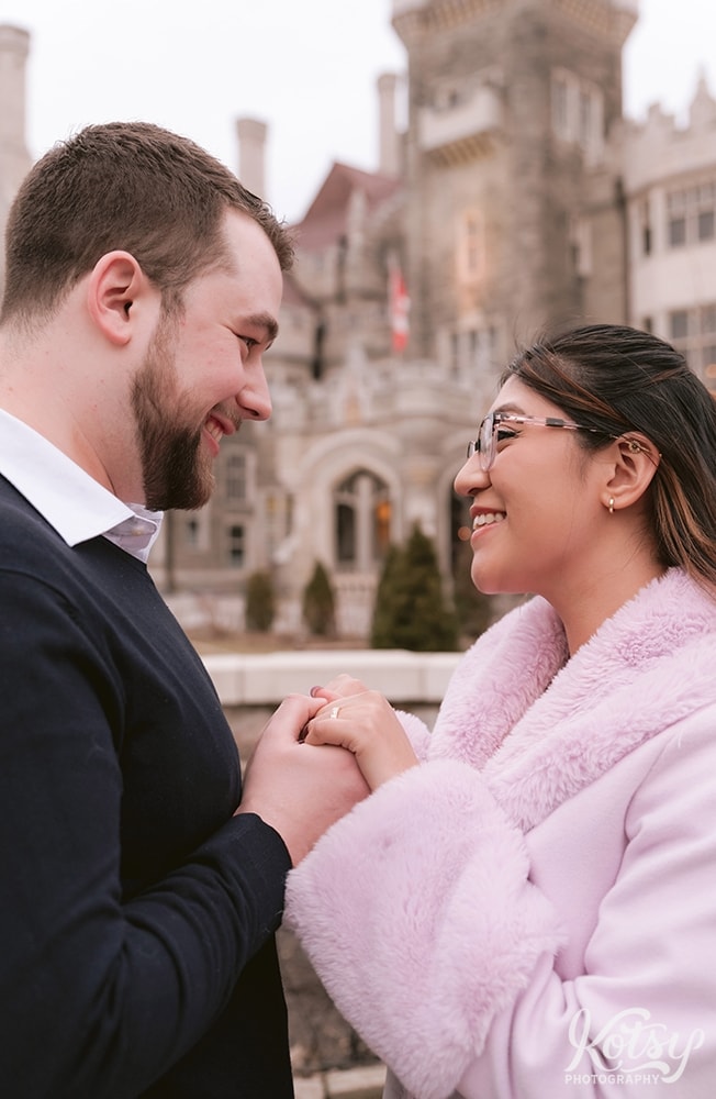 A man holds his newly engaged partner's hands in front of Casa Loma in Toronto