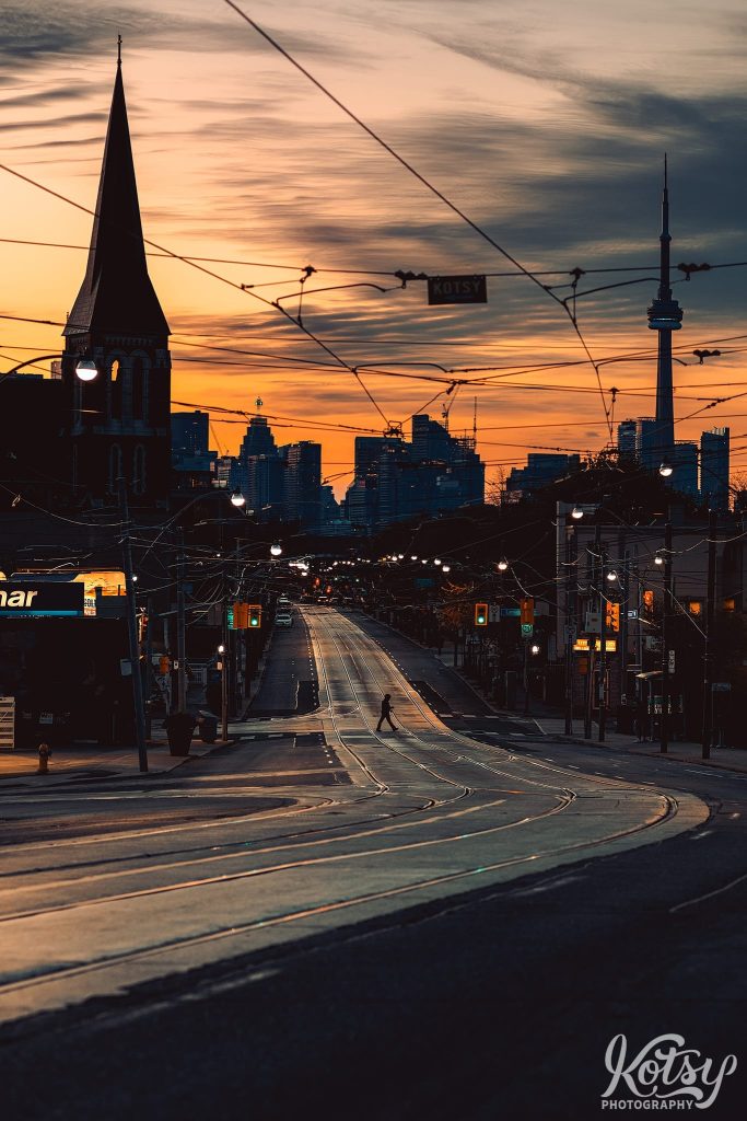 A pedestrian crosses an empty Dundas Street West in Toronto during sunrise