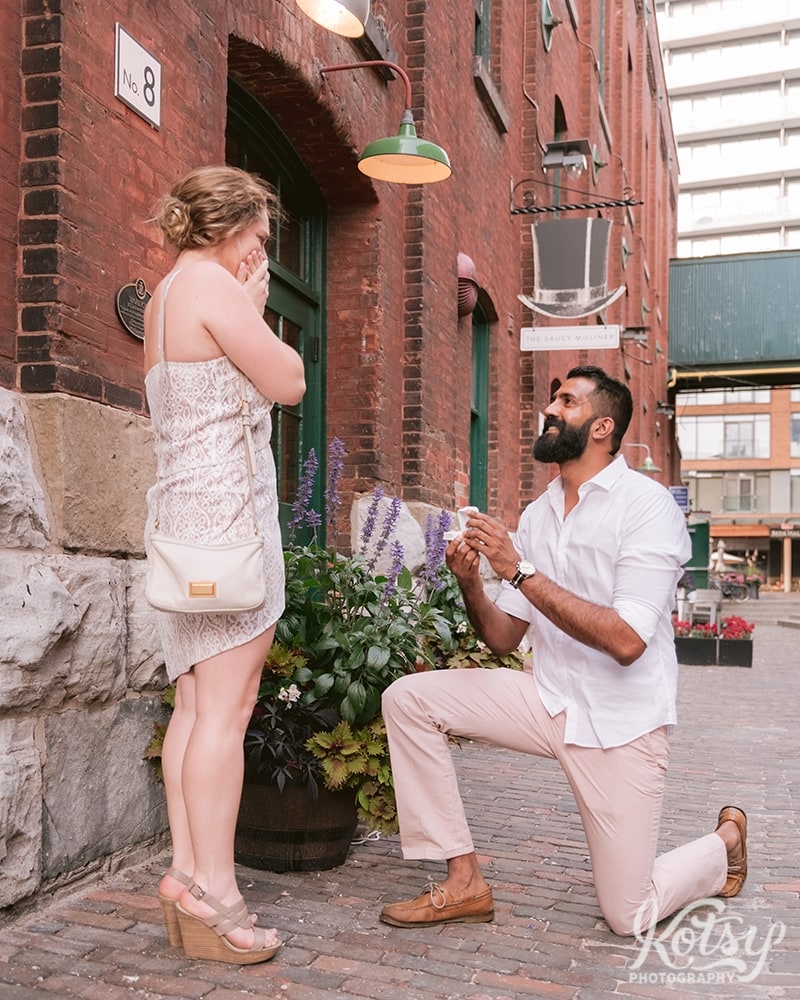 A man proposes to his girlfriend who has covered her mouth in shock. Photographed at The Distillery District in Toronto