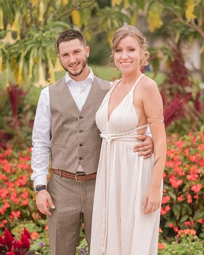 A newly married couple pose for a photo in front of a lush garden.