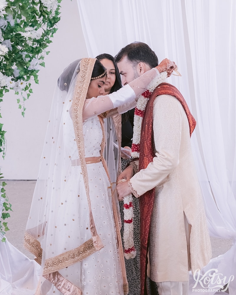 A bride puts an jai mala on her groom during their wedding ceremony at Guild Inn Estate