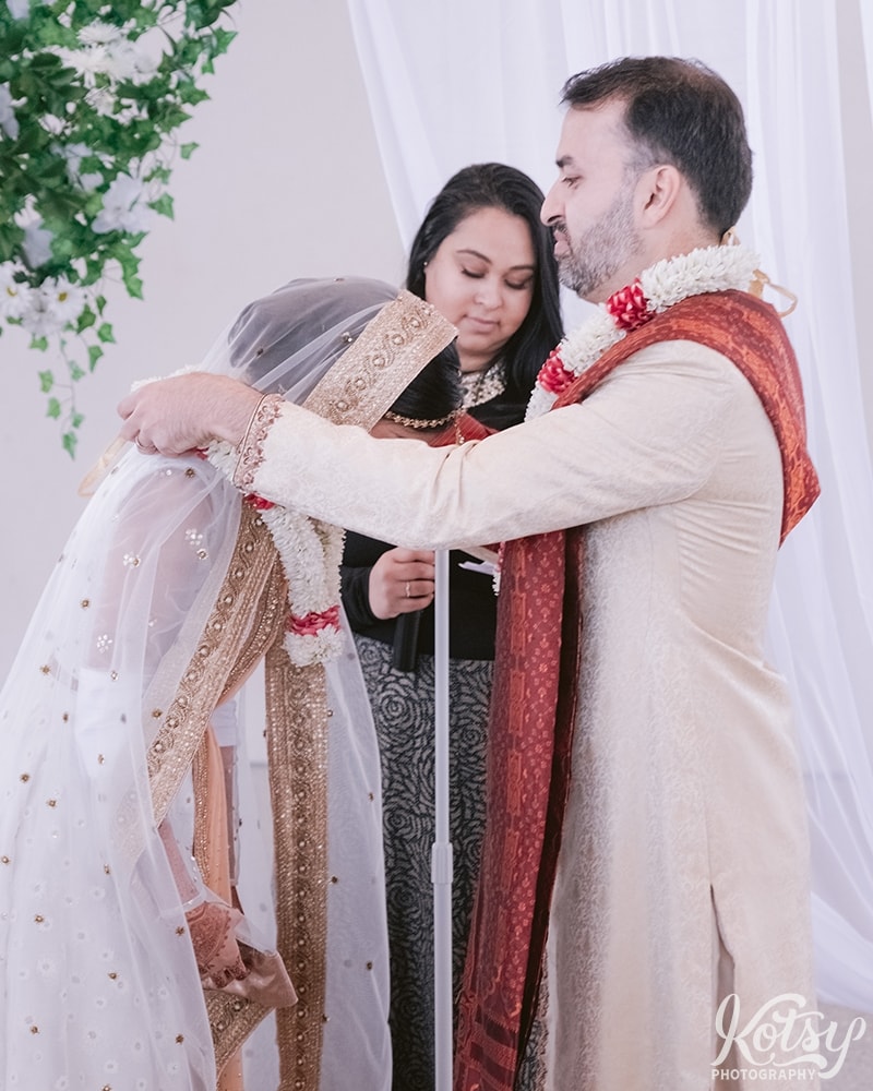 A groom puts a jai mala on his groom at their wedding ceremony at Guild Inn Estate