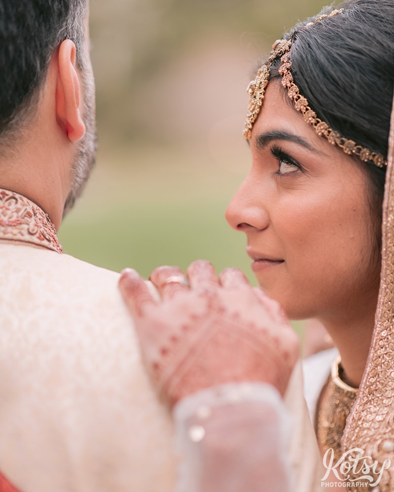 A close up shot of a groom's shoulder with his bride's hand resting on it while she stares at him with love.