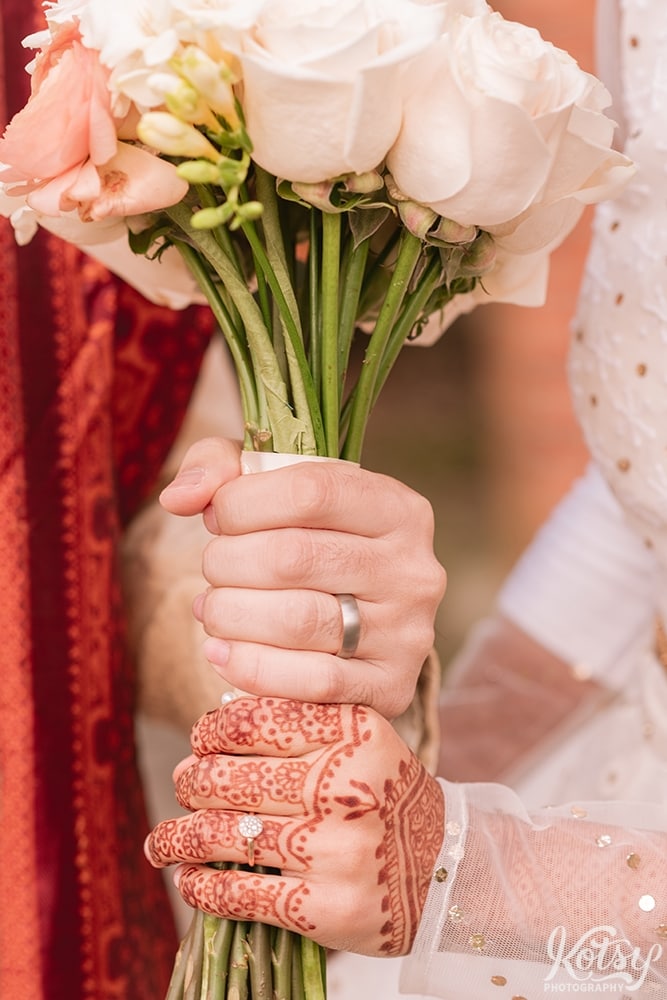 A close up shot of a bride and groom holding a bouquet of flyers. Their wedding rings are also seen. Photographed at Guild Park and Gardens