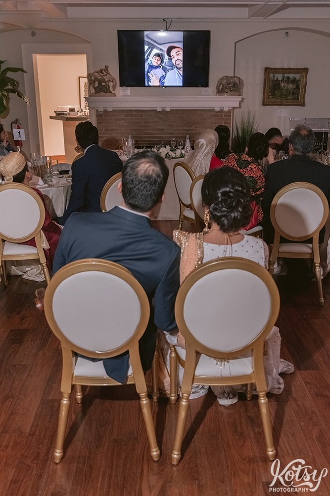 A bride and groom watch a video of family members recording a tribute to them at their wedding reception.