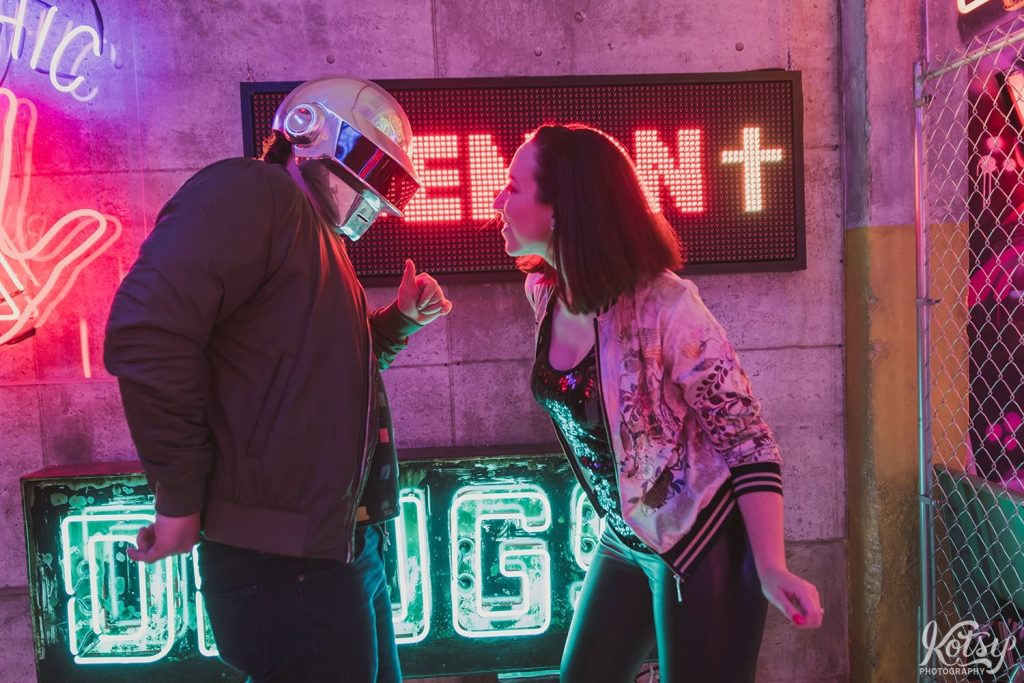 A recently engaged couple dance by neon signs at Neon Demon Studio in Toronto, Ontario
