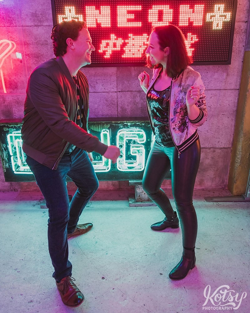 A recently engaged couple dance by neon signs at Neon Demon Studio in Toronto, Ontario