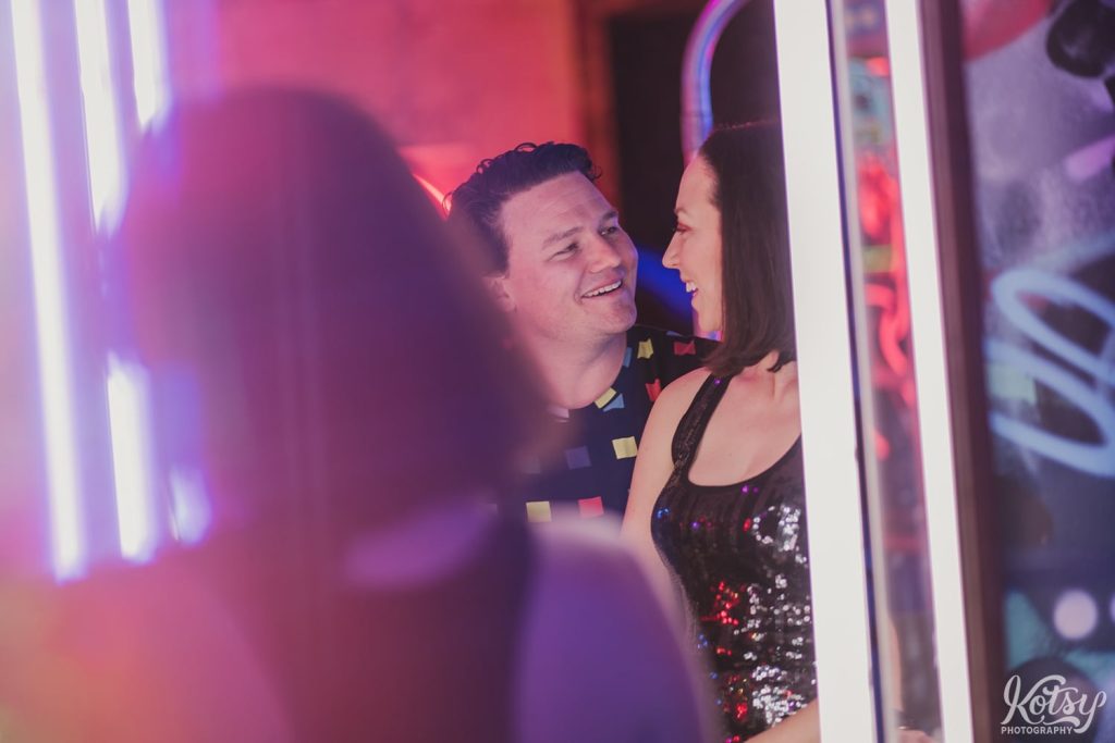 A recently engaged couple smile at each other, as seen through a mirror at Neon Demon Studio in Toronto