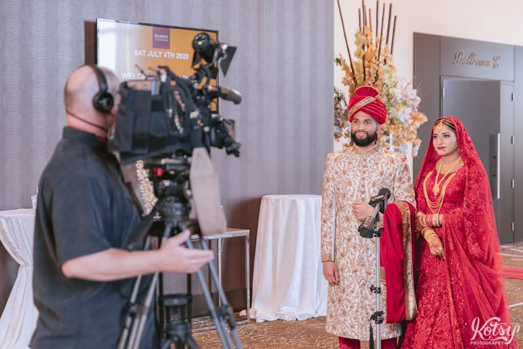 A bride and groom are interviewed behind a large television camera at the Pearson Convention Centre in Mississauga, Ontario