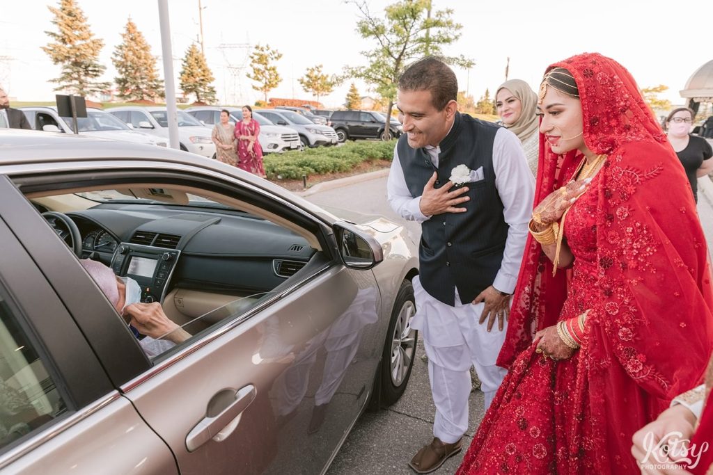 A bride and her father greet a related in a car during a drive-thru wedding. Photographed at the Pearson Convention Centre in Mississauga, Ontario