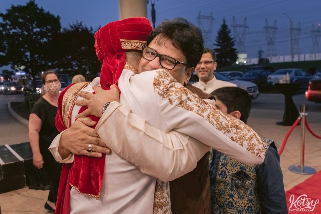 A man hugs a groom at a drive-thru wedding. Photographed at the Pearson Convention Centre in Mississauga, Ontario
