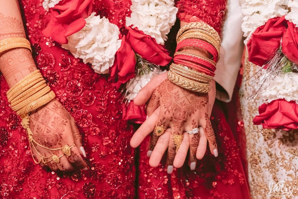 A close-up shot of a bride and groom holding hands. The bride's mehndi art and jewelry are seen.