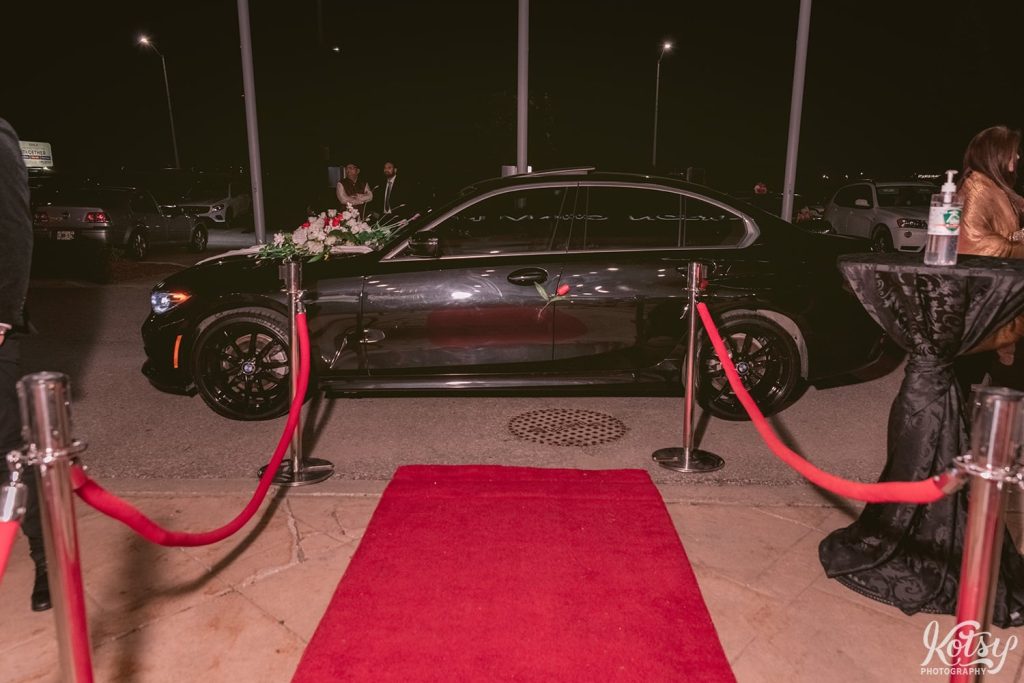A shot of a black BMW parked at the end of the red carpeted aisle at a drive-thru wedding. Photographed at the Pearson Convention Centre in Mississauga, Ontario
