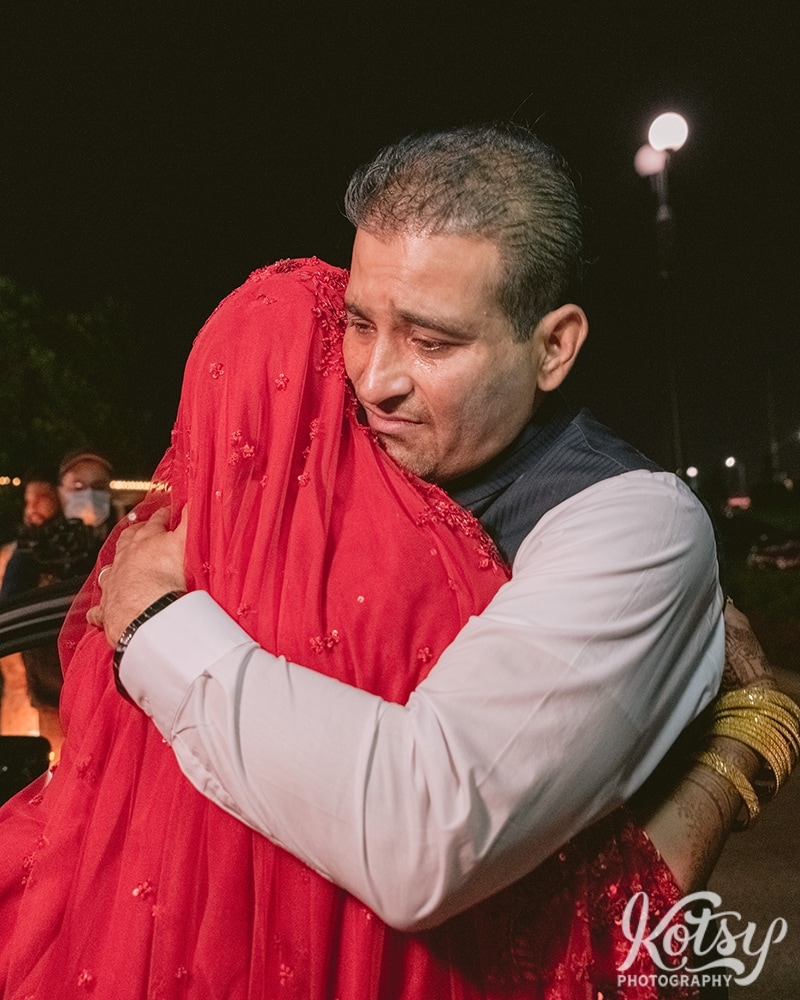 A man hugs his daughter bride as she makes her exit from a drive-thru wedding. Photographed at the Pearson Convention Centre in Mississauga, Ontario