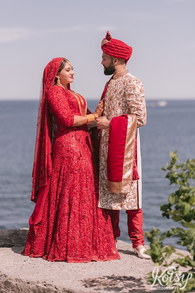 A bride and groom dressed in traditional south asian wedding attire exchange smiles at The Scarborough Bluffs