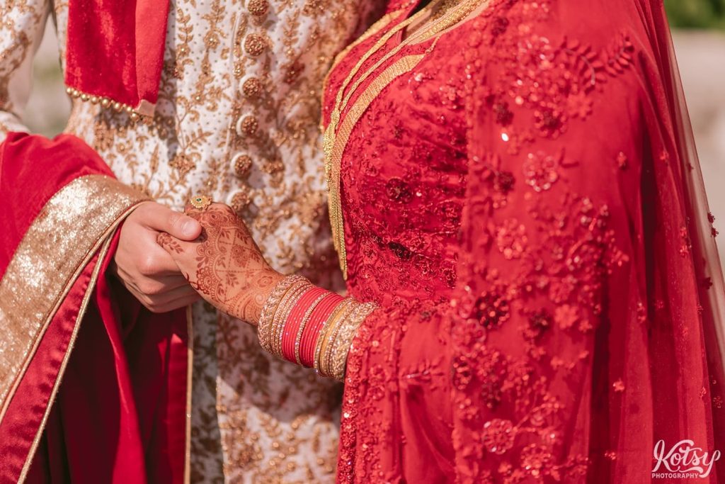 a close up shot of a bride and groom holding hands while wearing vibrant south asian wedding attire at The Scarborough Bluffs in Toronto