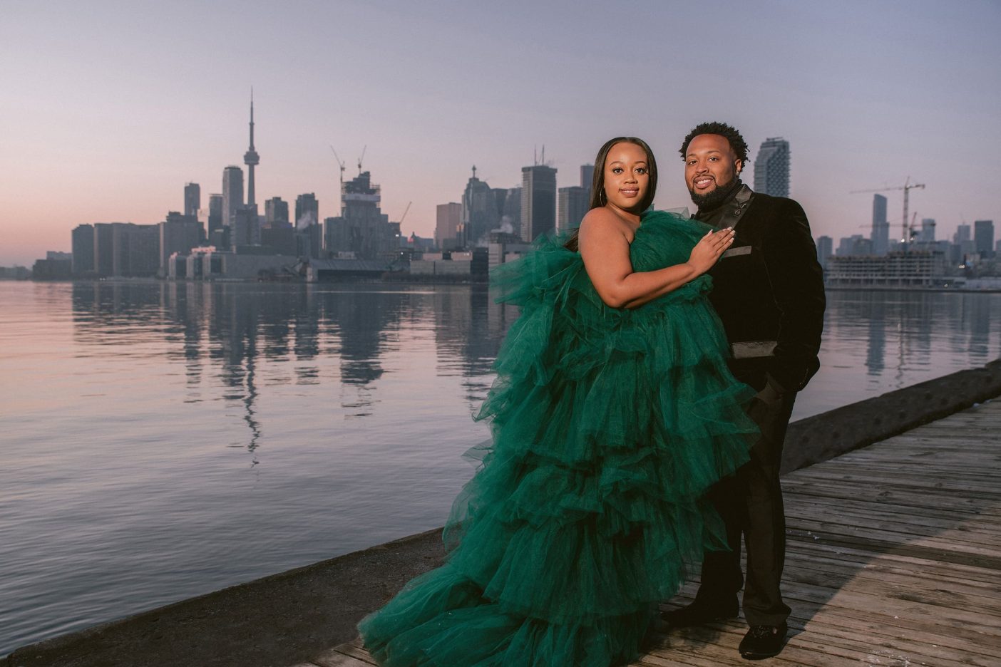 A recently engaged couple pose for a photo at Polson Pier in Toronto. The downtown skyline is seen in the background.