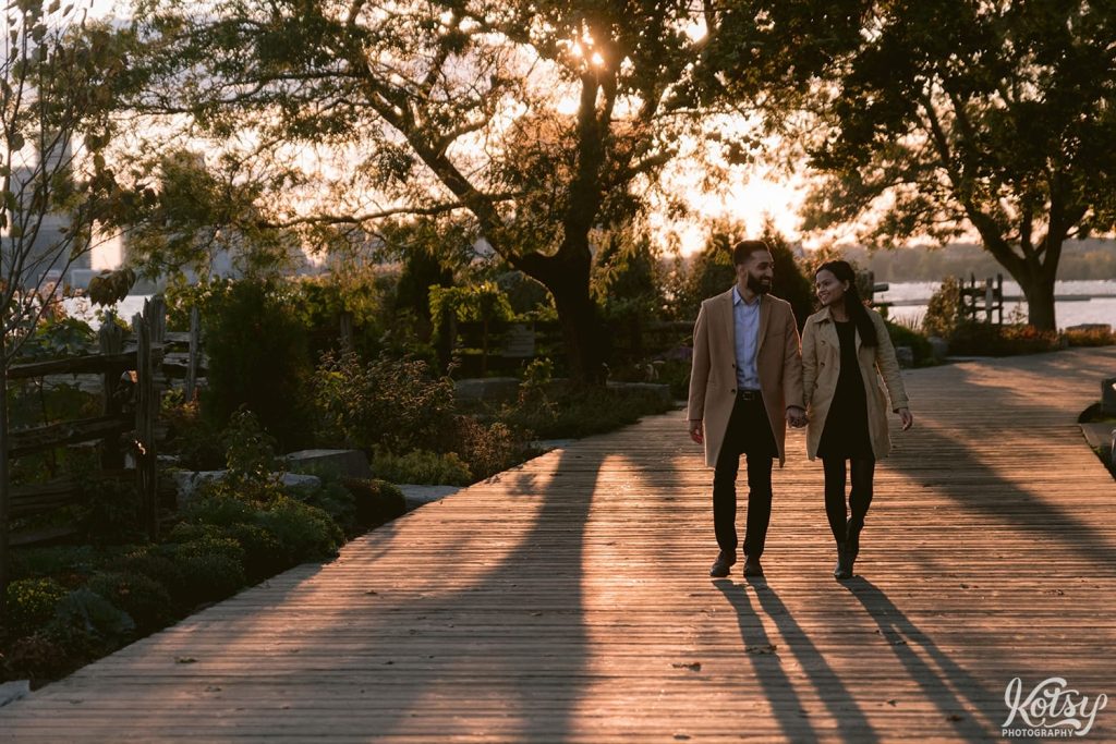 A man and woman walk hand-in-hand on the boardwalk on the Sunnyside Boardwalk at sunset in Toronto