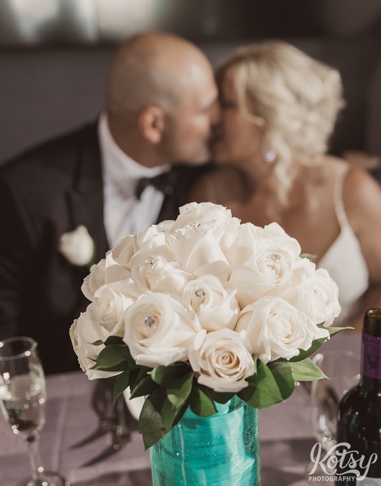 A close up shot of a flower bouquet with a bride and groom kissing in the distance.