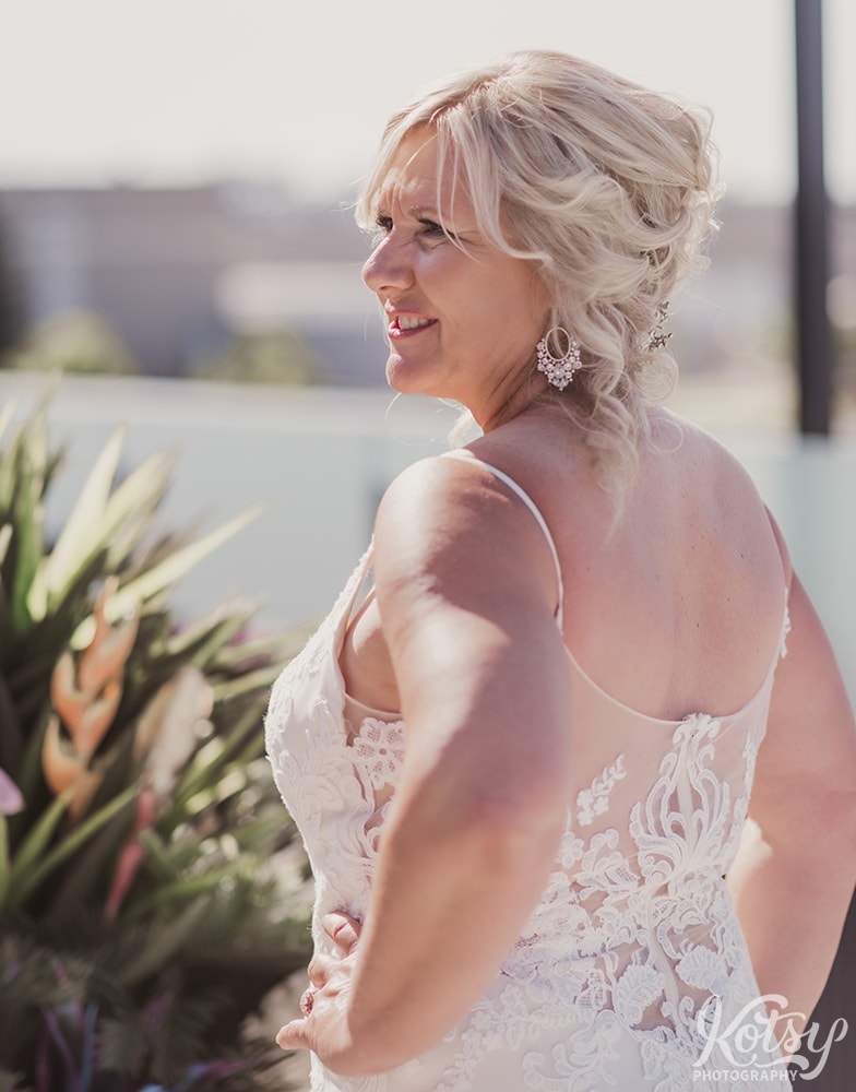 A shot from diagonally behind of a bride with one hand on her hip and a smile. Photographed on an outdoor patio at Universal EventSpace in Vaughan