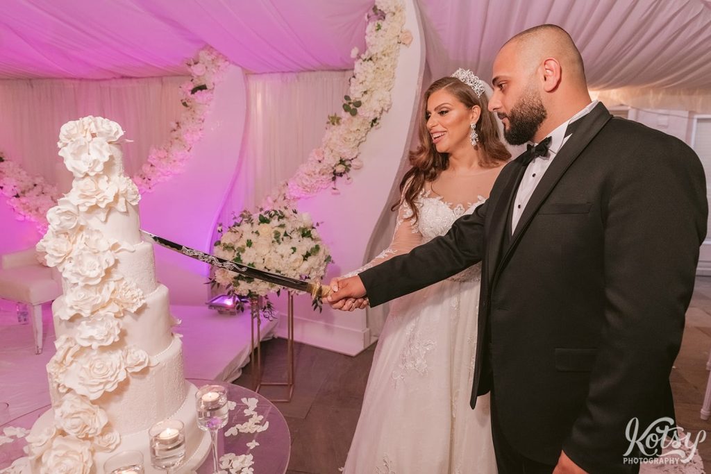 A bride and groom cut a 6 tier wedding cake with a massive sword