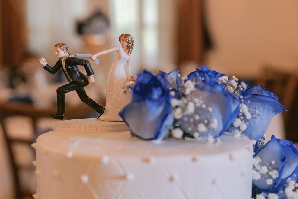 A close up shot of a wedding cake topper where the groom is trying to run from the bride.