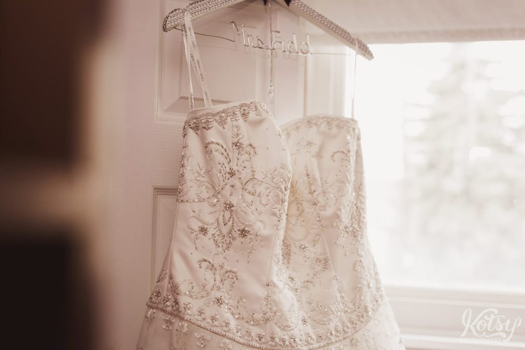 A close up shot of a wedding dress hanging on a door near a window
