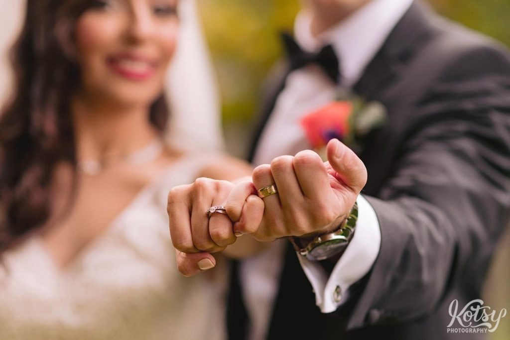 A close up shot of a bride and groom interlocking their fingers to show off their jewelry