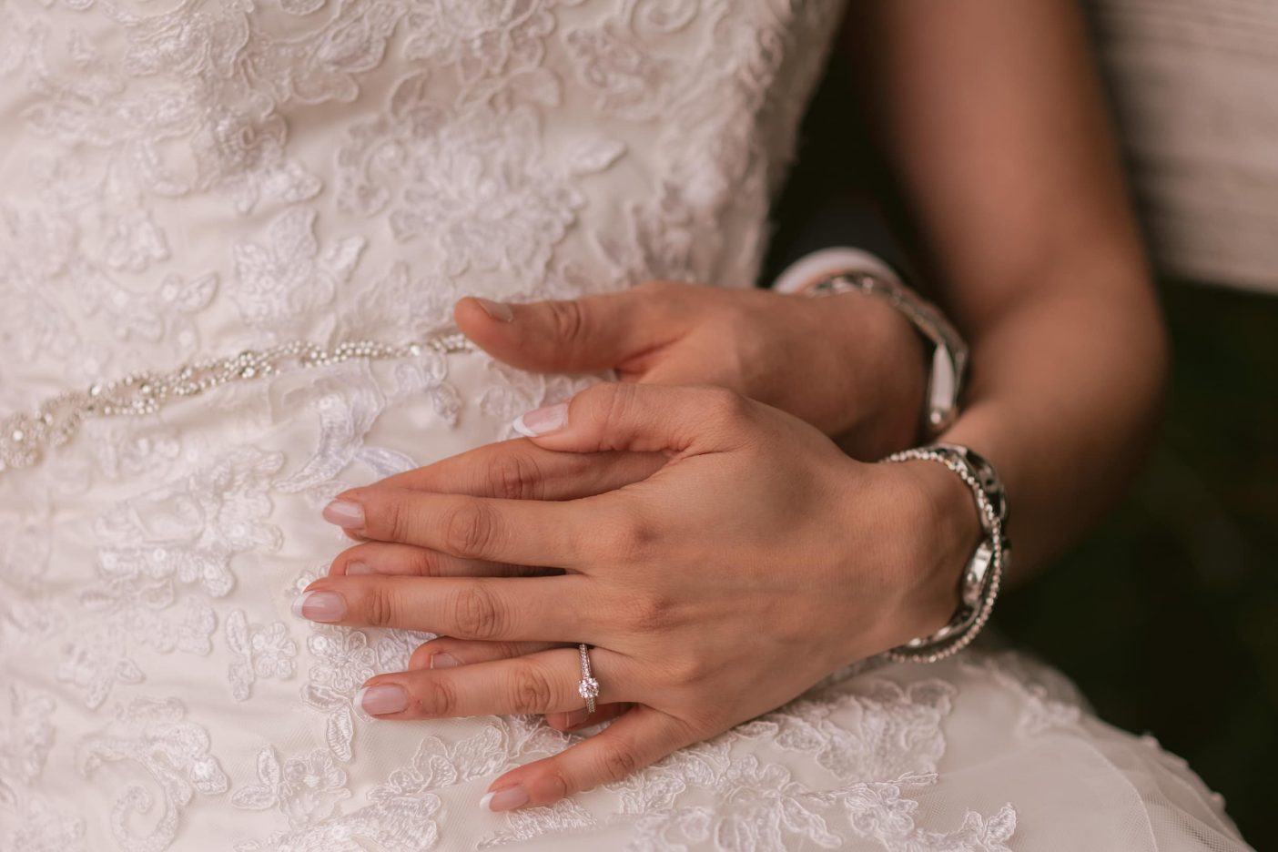 A bride and groom holds hands by her hip.