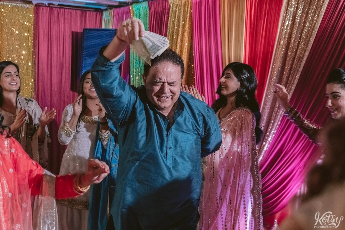 A man dressed in traditional South Asian clothing dancing while showing off a wad of cash.