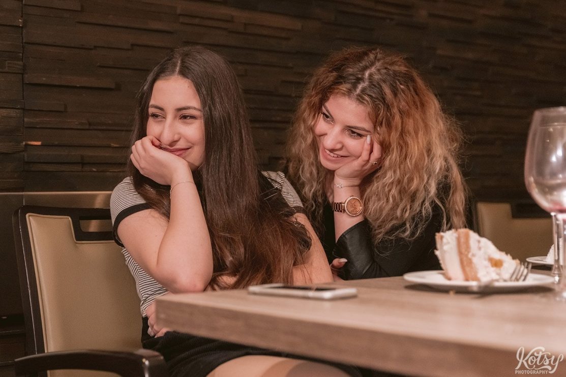 Two young women with big smiles watch a performance out of frame.