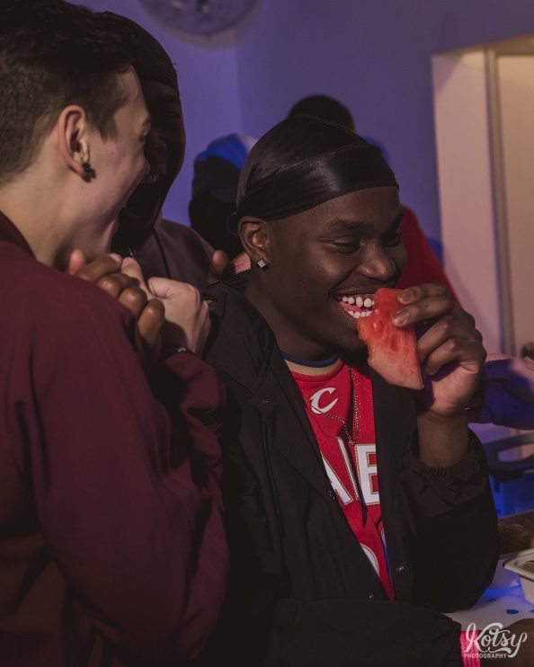 A young man enjoys a laugh while eating watermelon at a birthday party.