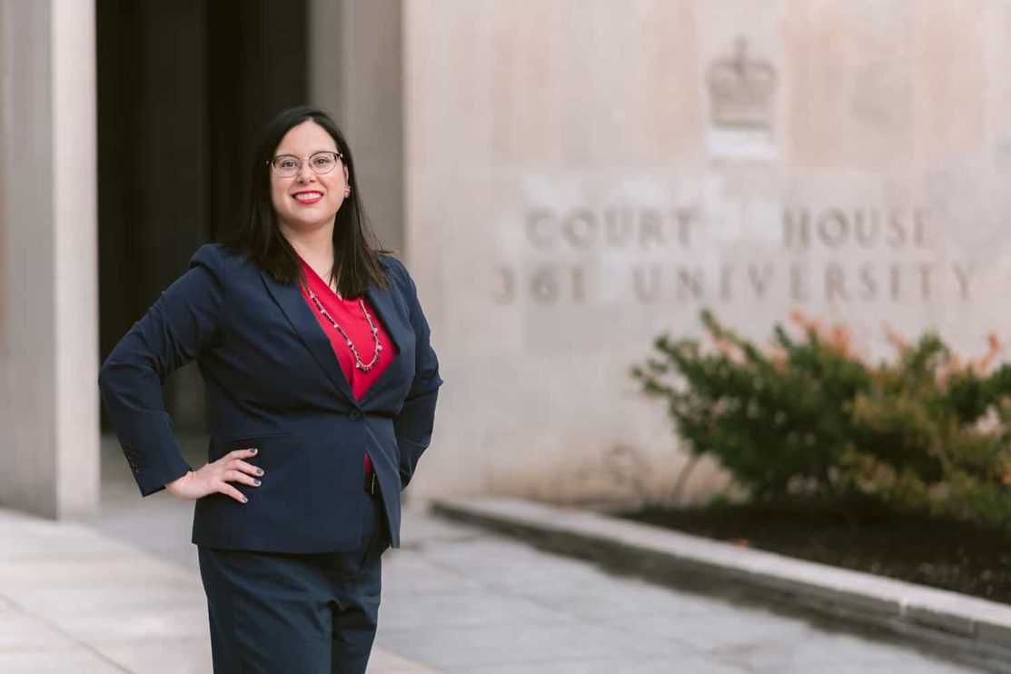 A woman dressed in a suit poses for a portrait in front a court house in Toronto