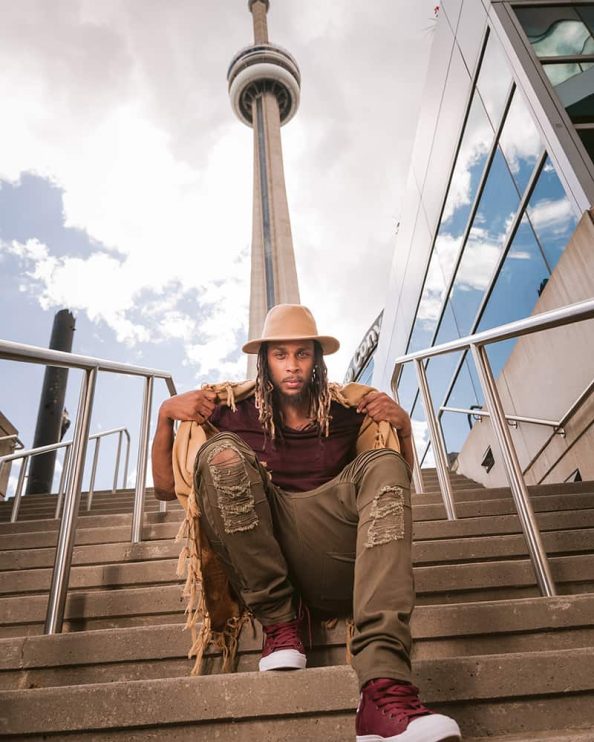 A low angle shot of a man posing for a portrait on a set of steps as the CN Tower rises behind him in Toronto