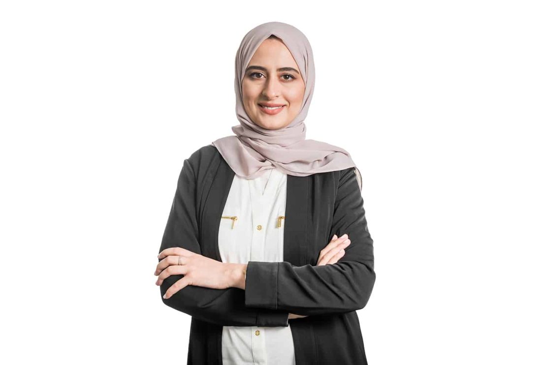 A woman wearing a headscarf poses for a portrait in front of a white background