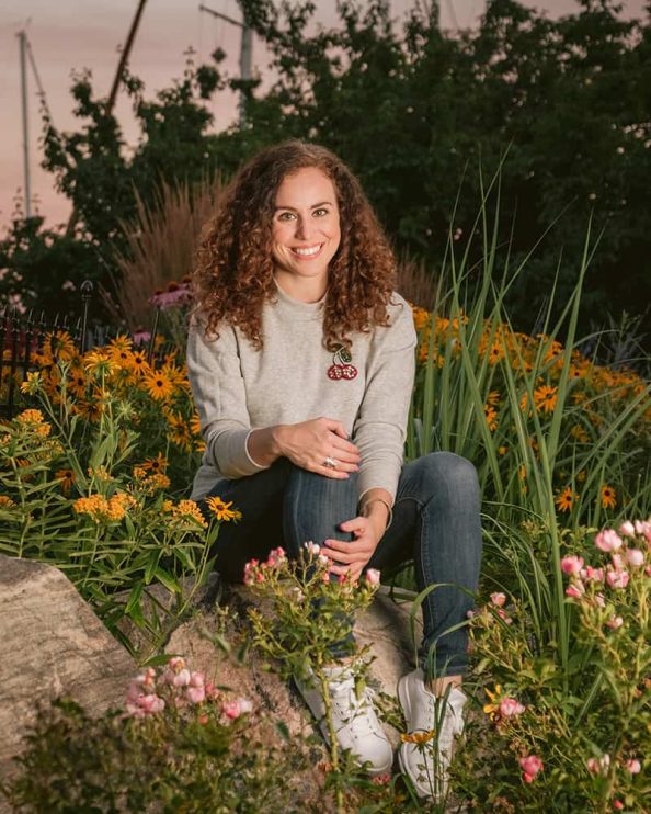 A woman poses for a portrait while sitting in on a rock in a garden in Toronto