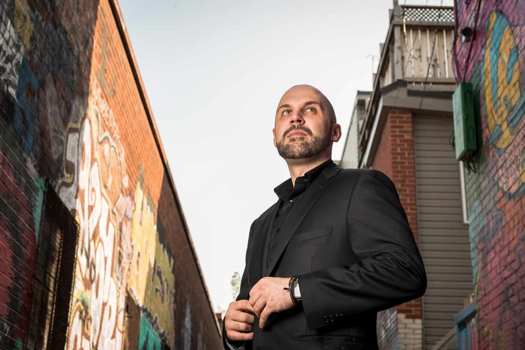 A low angle shot of a man buttoning up his blazer in a graffiti covered alley
