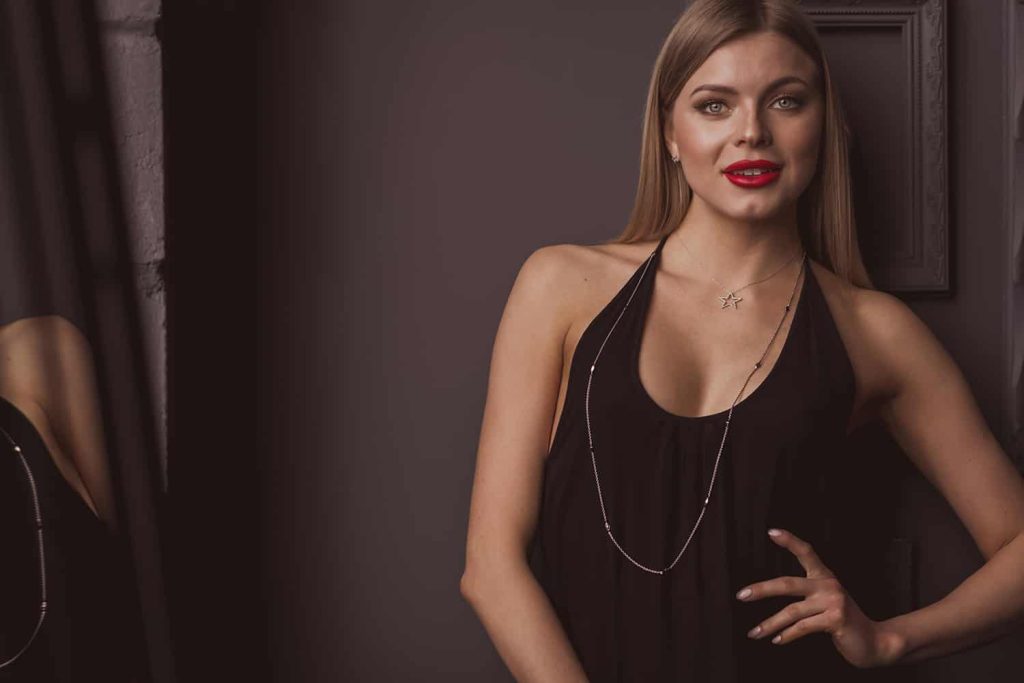 A woman poses for a portrait with a hand on her hip and long necklace and red lipstick