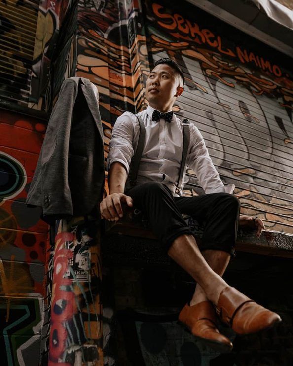 A low angle shot of a well dressed man with suspenders sitting on a loading dock covered in graffiti