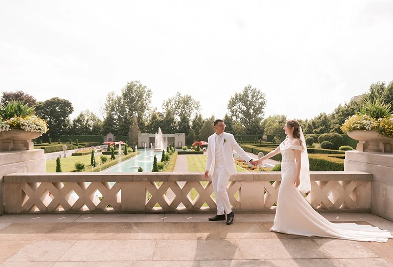 A groom guides his new bride while walking on a stone terrace