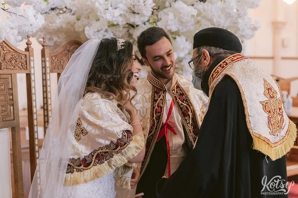 A bride and groom exchange a laugh with a priest during their Egyptian wedding ceremony at St Mary & St John Coptic Church
